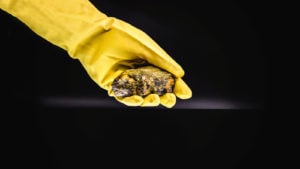 CCJ Stock: Hand in long yellow glove holding a chunk of uranium material