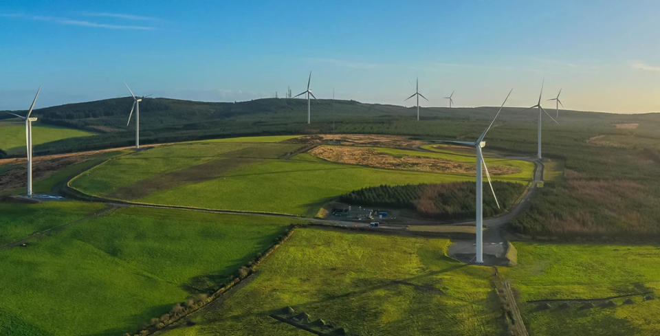 Green plains filled with large windmills. Blue sky.