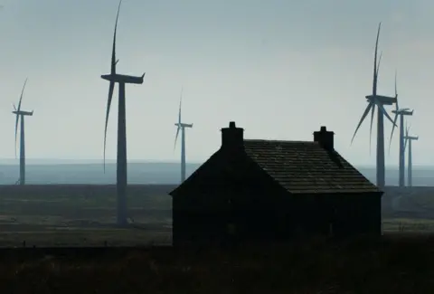 PA Media A Scottish cottage with turbines and the sea behind