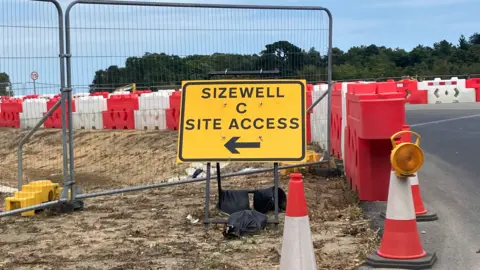 Guy Campbell/BBC Yellow road sign pointing to Sizewell C site access behind three red and white cones 