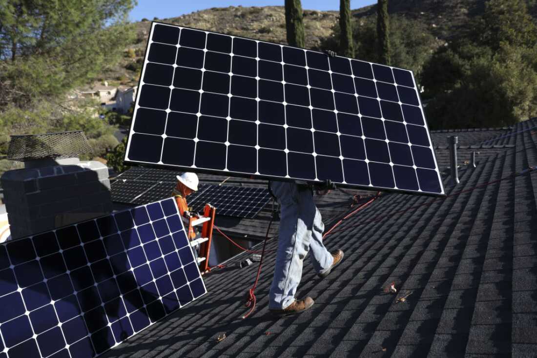 Workers install solar panels on the rooftop of a home in Poway, California.