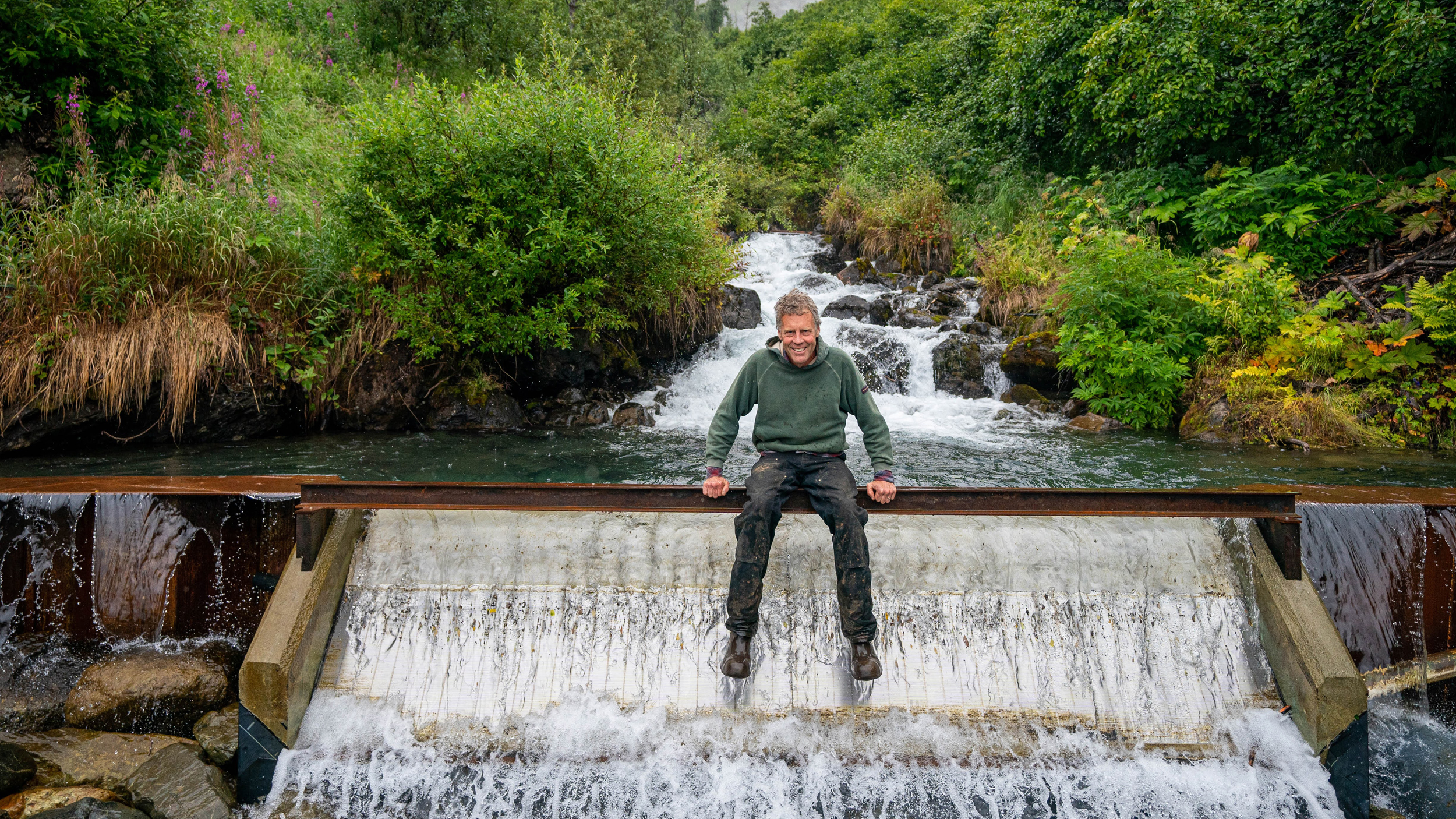 Hydrologist David Brailey developed a small hydro project that generates power from water flowing down a Chugach Mountain creek. Here, he sits above a spillway that collects the water for the 300-kilowatt project. Credit: Loren Holmes/ADN