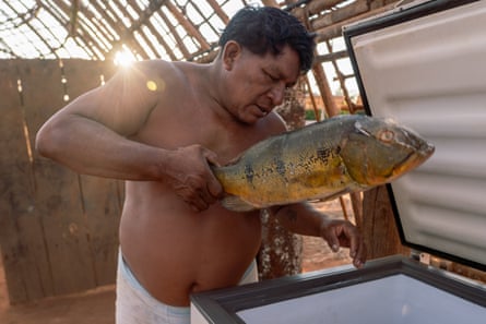 A man holding a frozen fish next to a freezer in a partly built hut