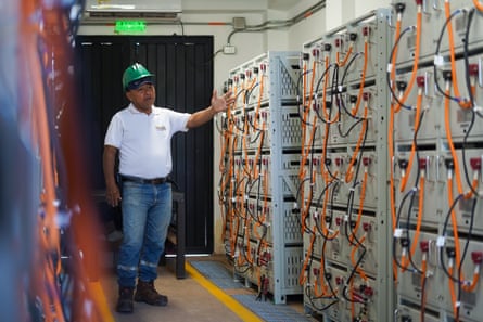 A man in a hard hat stands next to an indoor wall of metal boxes with wires protruding