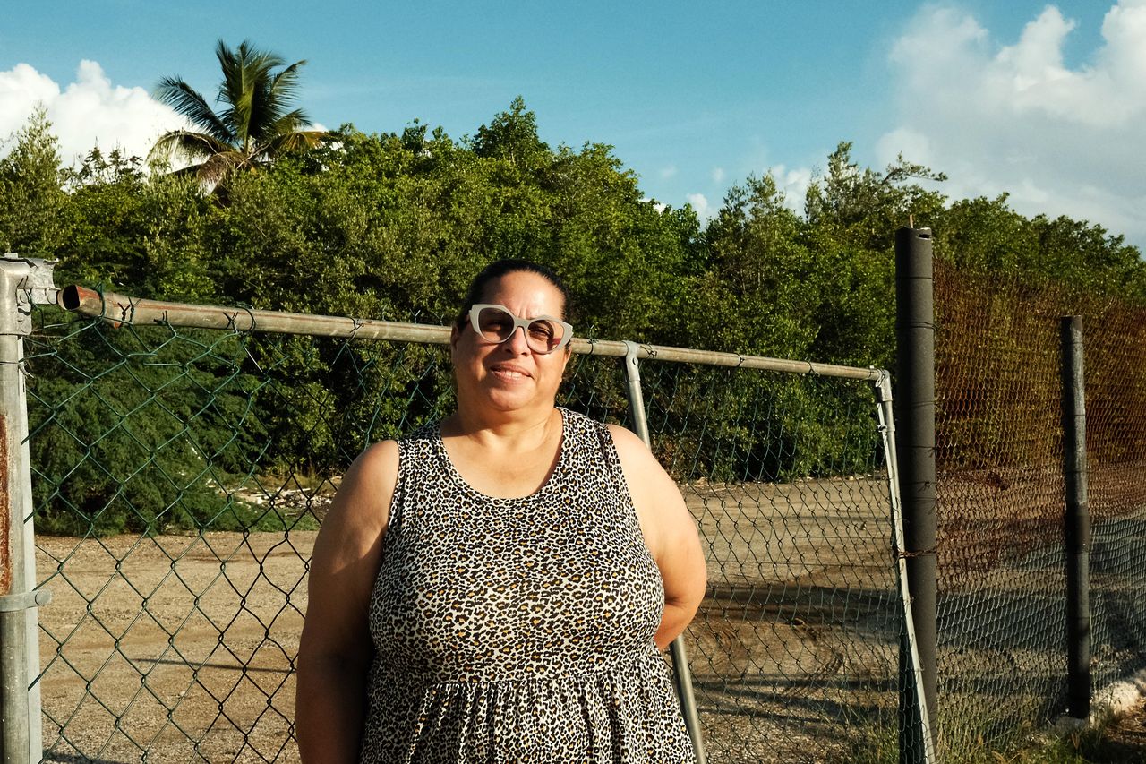 Adneris Hernández stands outside her home in the Mosquito neighborhood of Salinas, Puerto Rico, which is in a flood zone. She expects to experience hardship from a new federally backed solar farm set to begin construction nearby.