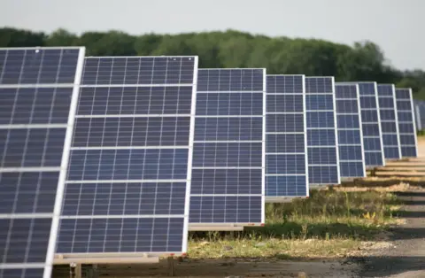 PA Media A line of blue solar panels on a grassy field