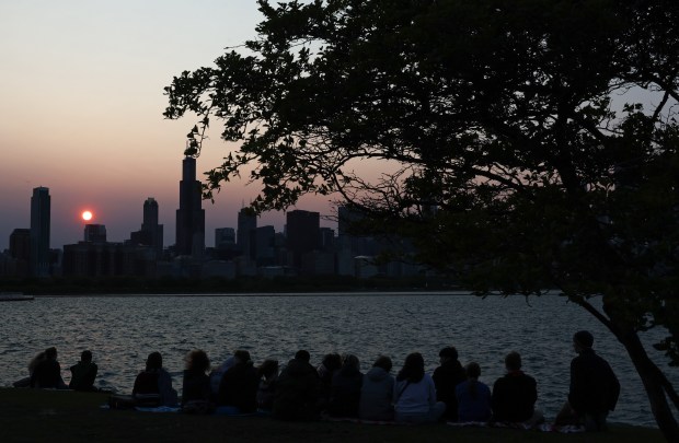 A group of youths watch the sun set behind the skyline from East Solidarity Drive,on May 17, 2023, in Chicago. Smoke from Canadian wildfires has dimmed the brightness of the sun. (John J. Kim/Chicago Tribune)