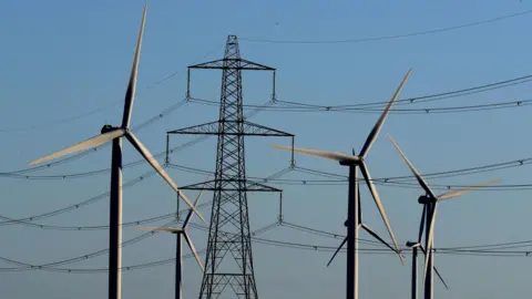 PA Media Wind farm turbines and electricity pylons on the Romney Marsh in Kent.