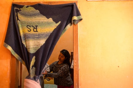 A young Latina woman seen through a doorway with a blanket hung up over it as a makeshift door